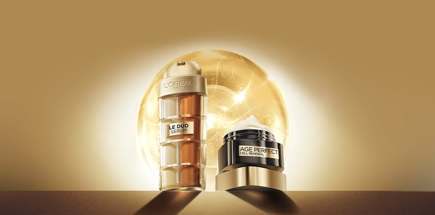 Opakowania serum Le Duo oraz kremu Age Perfect Cell Renewal stojące na złotym podeście na tle złotej, iskrzącej się molekuły