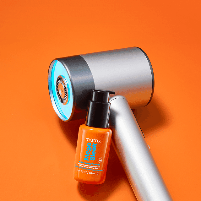 Serum Matrix Mega Sleek oparte o nowoczesną suszarkę na pomarańczowym tle. Podpis: 'Krok 3 Wystylizuj włosy.'