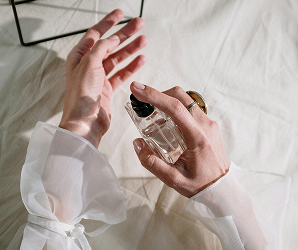 Perfumy – dłonie trzymające elegancki flakon perfum na jasnym tle.